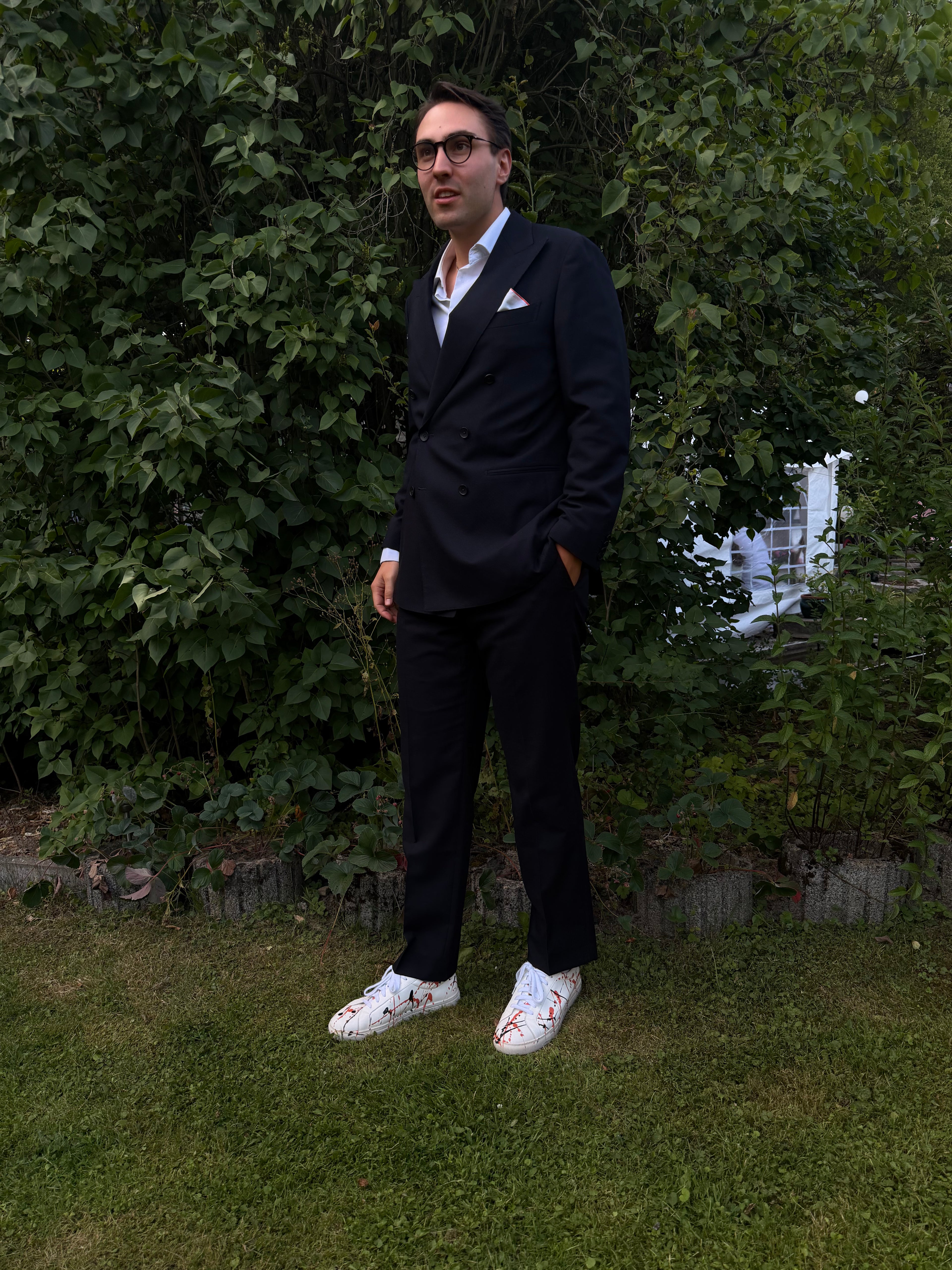 im anzug mit signal sneaker im Garten vor einer Hecke auf dem rasen, junger mann
